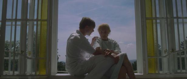 Ein junger Mann tröstet eine ältere Frau am Fenster.