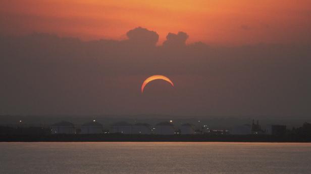 Eine ringförmige Sonnenfinsternis über dem Wasser bei Sonnenuntergang.
