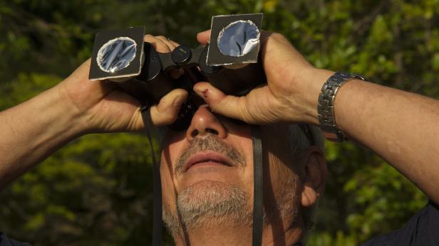 Ein Mann mit Bart und Sonnenfilter-Fernglas blickt in den Himmel.