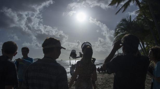 Eine Filmcrew filmt eine Szene am Strand unter bewölktem Himmel.