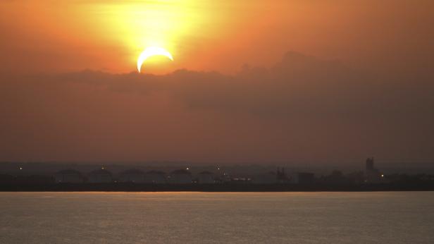 Eine partielle Sonnenfinsternis über einer Küstenlandschaft bei Sonnenuntergang.