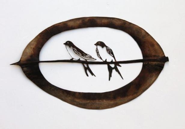 Zwei stilisierte Schwalben sitzen auf einem Ast, umrahmt von einem Blatt.