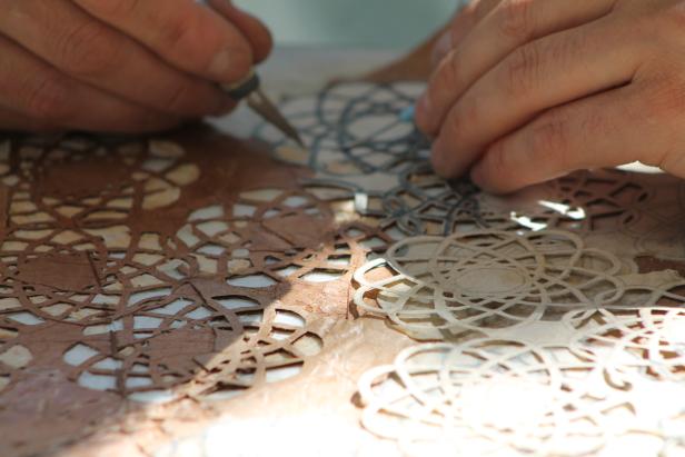 Ein Handwerker schneidet mit einem Werkzeug filigrane Muster in ein Material.