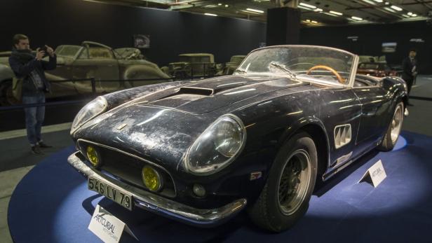 Ein schmutziger, schwarzer Ferrari steht auf einer blauen Ausstellungsfläche.