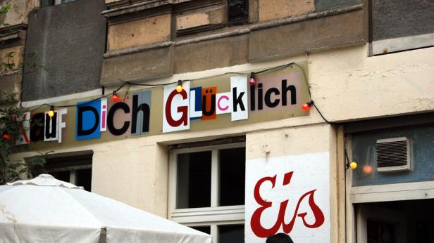 Ein Schild mit der Aufschrift „Kauf Dich Glücklich“ hängt über einem Laden.
