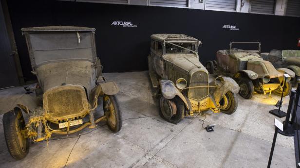 Drei alte, verstaubte Autos stehen in einer Ausstellungshalle.