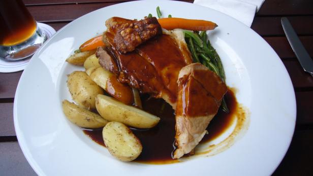 Ein Teller mit Braten, Kartoffeln, grünen Bohnen und Karotten mit dunkler Soße.