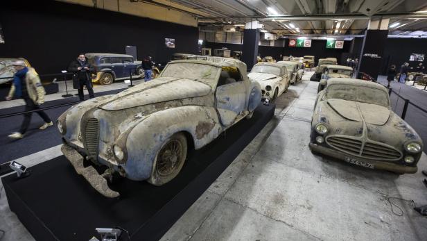 Eine Reihe von Oldtimern steht in einer Halle, bedeckt mit Staub und Schmutz.