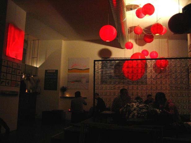 Ein Innenraum mit roter Beleuchtung und mehreren Personen an Tischen.