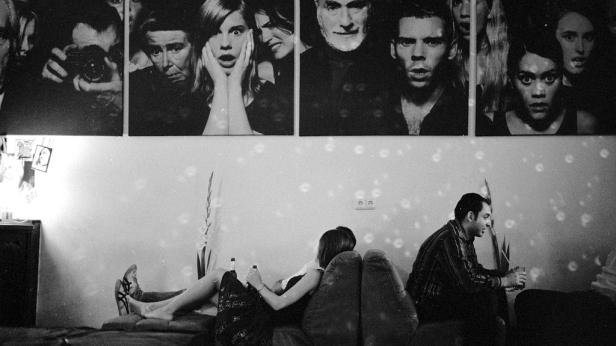 Schwarzweißaufnahme einer Party mit Menschen auf einem Sofa unter Porträtkunst.