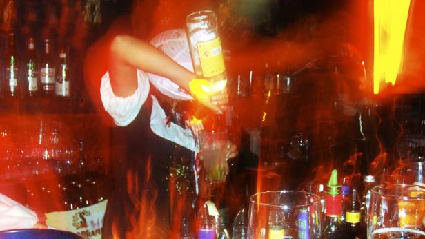 Ein Barkeeper mixt einen Drink in einer Bar mit roter Beleuchtung.