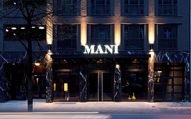 Das beleuchtete „MANI“-Schild über dem Eingang eines Hotels bei Nacht.