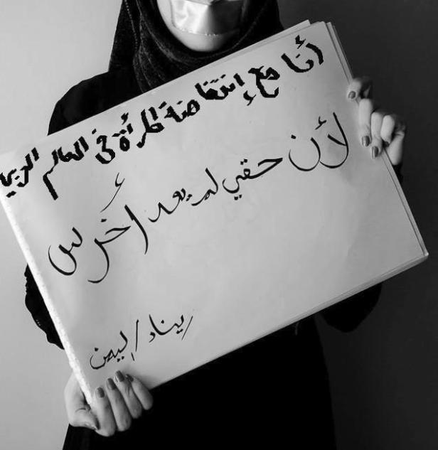 Eine Frau mit verklebtem Mund hält ein Schild mit arabischer Schrift hoch.