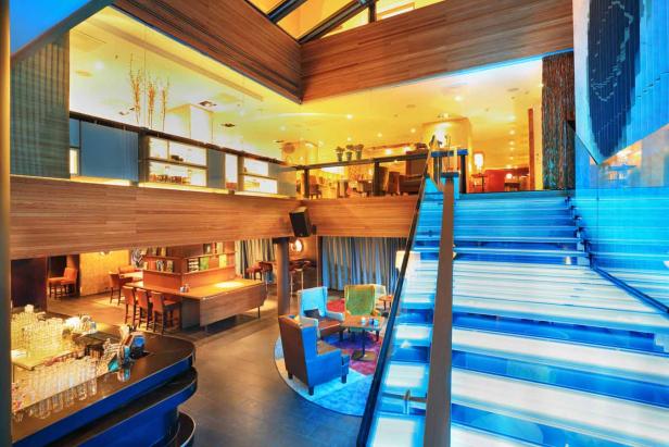 Mehrere Ebenen eines modernen Loungebereichs mit Bar und beleuchteter Treppe.