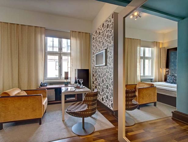 Ein Hotelzimmer mit Sessel, Tisch und Blick auf das Schlafzimmer durch einen Spiegel.