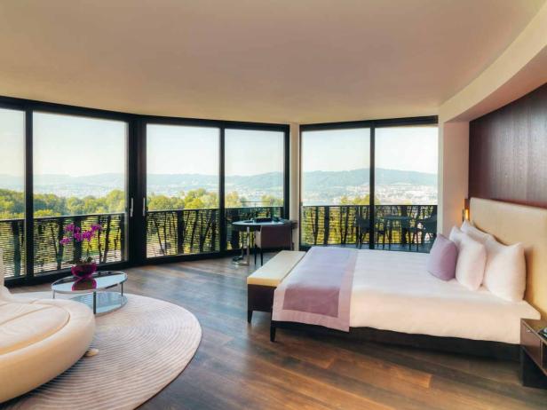 Ein helles Hotelzimmer mit Panoramablick auf eine Stadt und einen See.