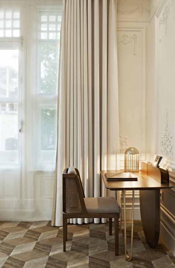 Ein Schreibtisch mit Stuhl steht vor einem Fenster mit Vorhängen.