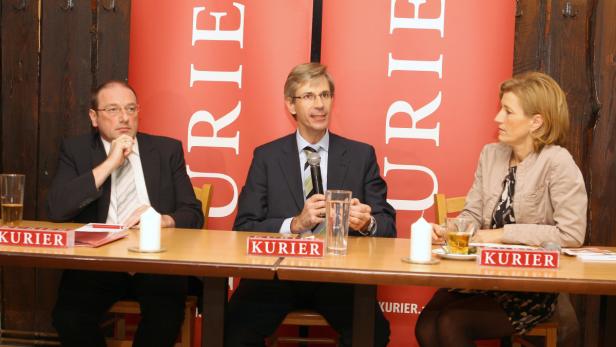 Drei Personen sitzen an einem Tisch mit dem „Kurier“-Logo im Hintergrund.