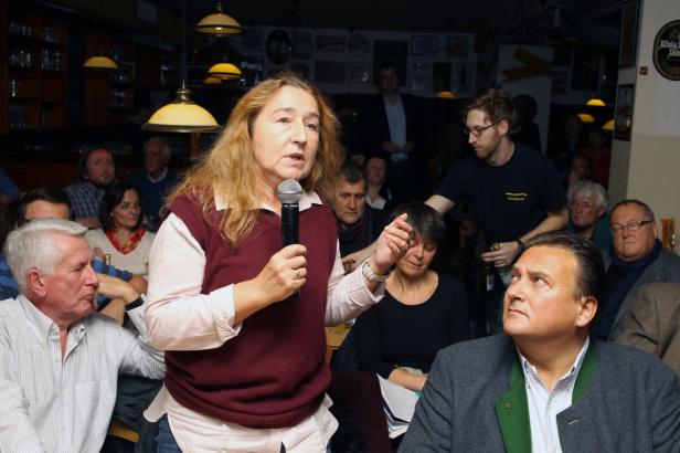 Eine Frau spricht mit einem Mikrofon vor einem Publikum in einem Raum.