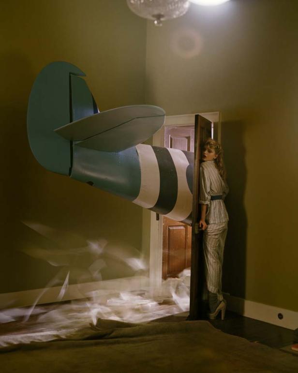 Der hintere Teil eines Flugzeugs ragt in ein Zimmer, in dem eine Frau aus einer Tür schaut.