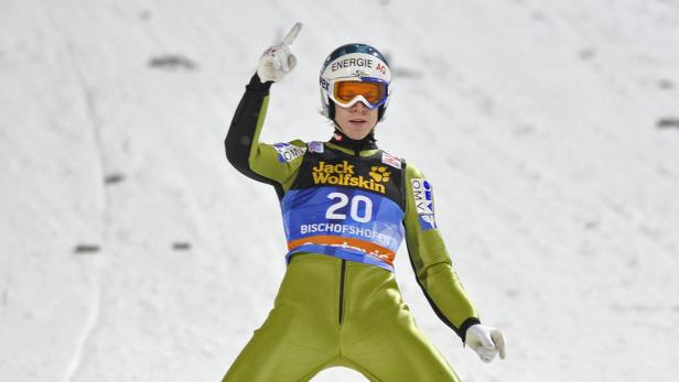 Ein Skispringer in grüner Kleidung und mit Startnummer 20 jubelt mit erhobenem Zeigefinger.