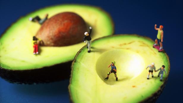 Miniaturfiguren bevölkern zwei halbe Avocados, einige skaten und laufen.