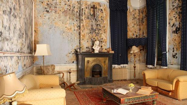 Ein heruntergekommenes Wohnzimmer mit abblätternder Farbe und antiken Möbeln.