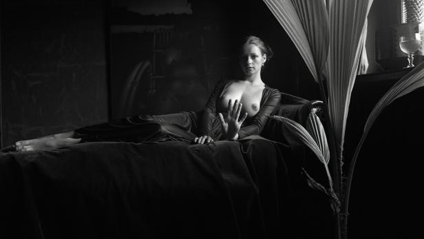 Eine Frau liegt in einem dunklen Raum auf einem Sofa und streckt die Hand aus.