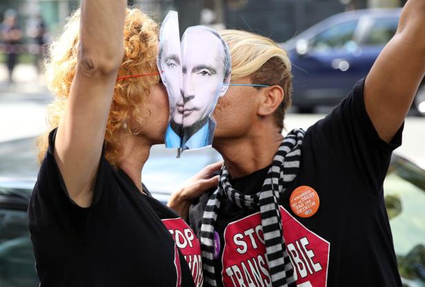 Zwei Personen mit „Stop Transphobie“-Shirts küssen eine Putin-Maske.
