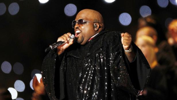 CeeLo Green tritt in einem glitzernden schwarzen Gewand mit Sonnenbrille auf einer Bühne auf.