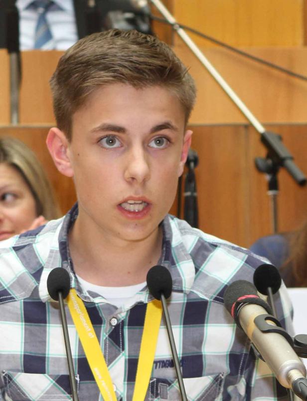 Ein junger Mann spricht bei einer Veranstaltung in mehrere Mikrofone.