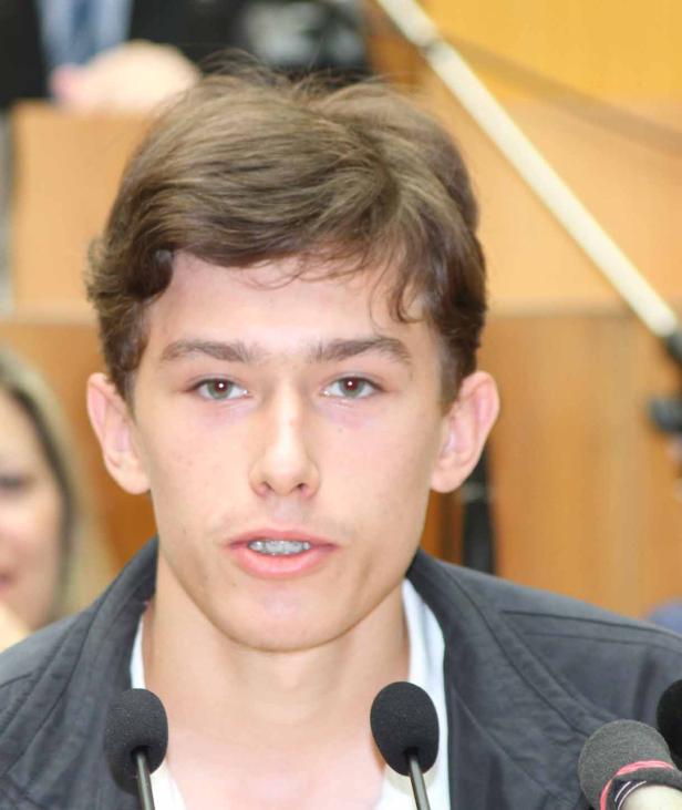 Ein junger Mann spricht vor mehreren Mikrofonen.