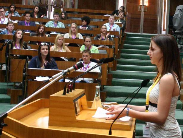 Eine junge Frau hält eine Rede vor einem Publikum in einem Hörsaal.