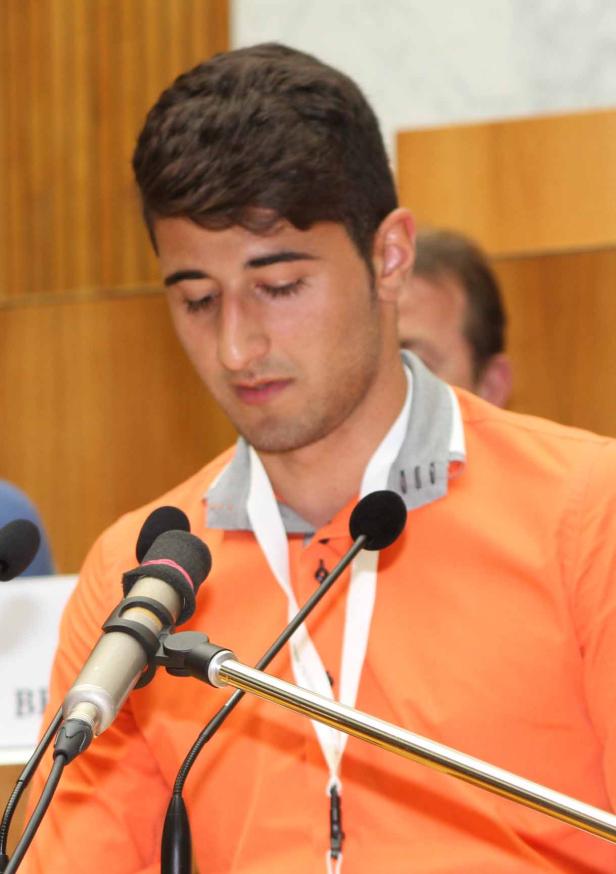 Ein junger Mann spricht bei einer Konferenz vor mehreren Mikrofonen.