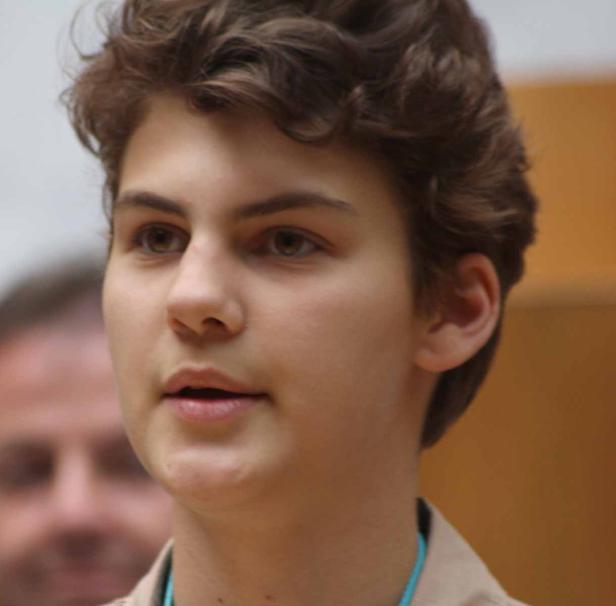 Ein junger Mann mit braunen, lockigen Haaren schaut aufmerksam zur Seite.