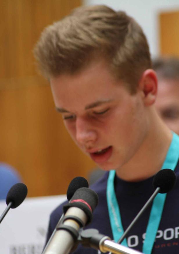 Ein junger Mann spricht vor mehreren Mikrofonen.