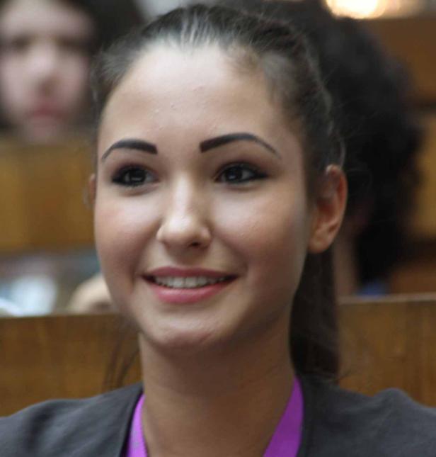 Eine lächelnde junge Frau mit dunklen Haaren und einem lila Band um den Hals.