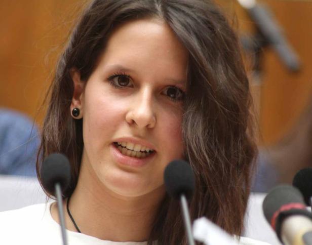 Eine junge Frau spricht vor mehreren Mikrofonen.