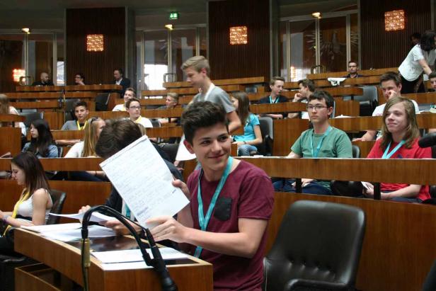 Jugendliche sitzen in einem holzvertäfelten Raum, möglicherweise bei einer Konferenz oder Simulation.
