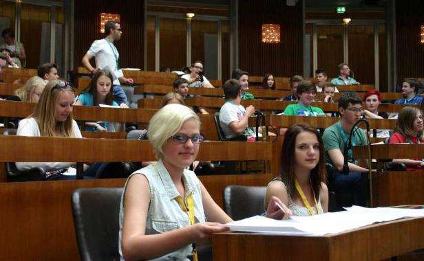 Zahlreiche junge Menschen sitzen in einem Hörsaal und hören aufmerksam zu.