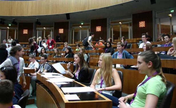 Jugendliche sitzen in einem halbrunden Raum mit Holzbänken und Tischen.