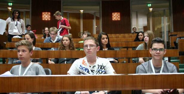 Eine Gruppe Jugendlicher sitzt in einem Hörsaal oder Konferenzraum.