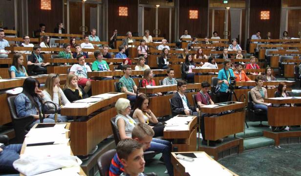 Zahlreiche Jugendliche sitzen in einem großen Saal mit Holzbänken.