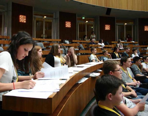 Jugendliche sitzen in einem halbrunden Raum und bearbeiten Papiere.