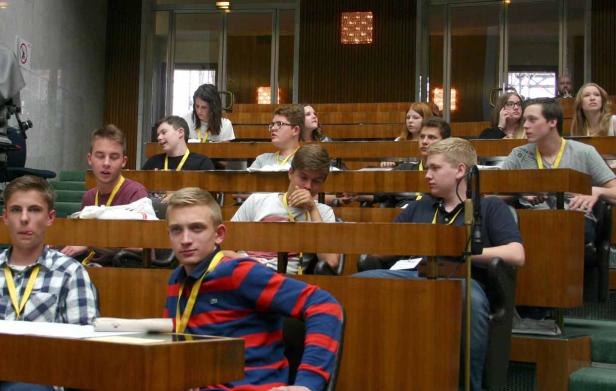 Eine Gruppe junger Leute sitzt in einem Hörsaal mit hölzernen Bänken.