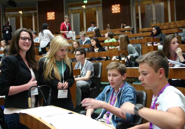 Jugendliche sitzen in einem großen Raum mit Holzbänken und diskutieren.