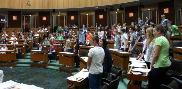 Eine Gruppe junger Menschen sitzt oder steht in einem großen Sitzungssaal.