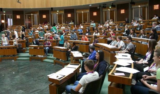 Viele Menschen sitzen in einem großen, halbrunden Raum mit Holzbänken.
