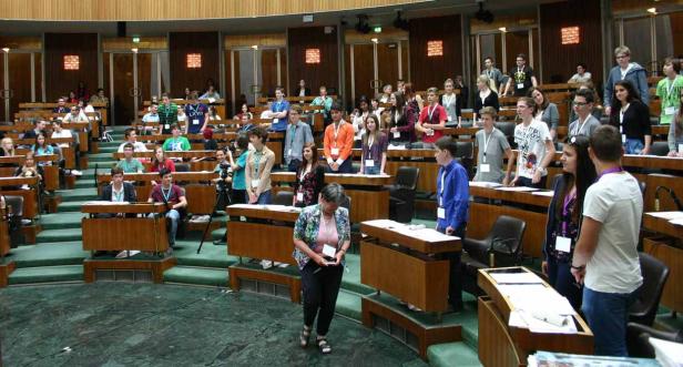 Eine Gruppe junger Menschen sitzt oder steht in einem großen Sitzungssaal.