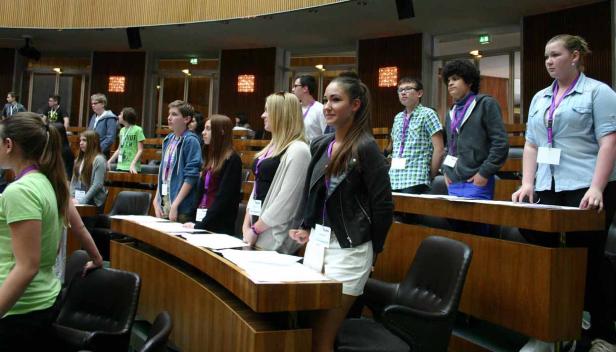 Eine Gruppe Jugendlicher steht in einem Sitzungssaal mit Holztäfelung.